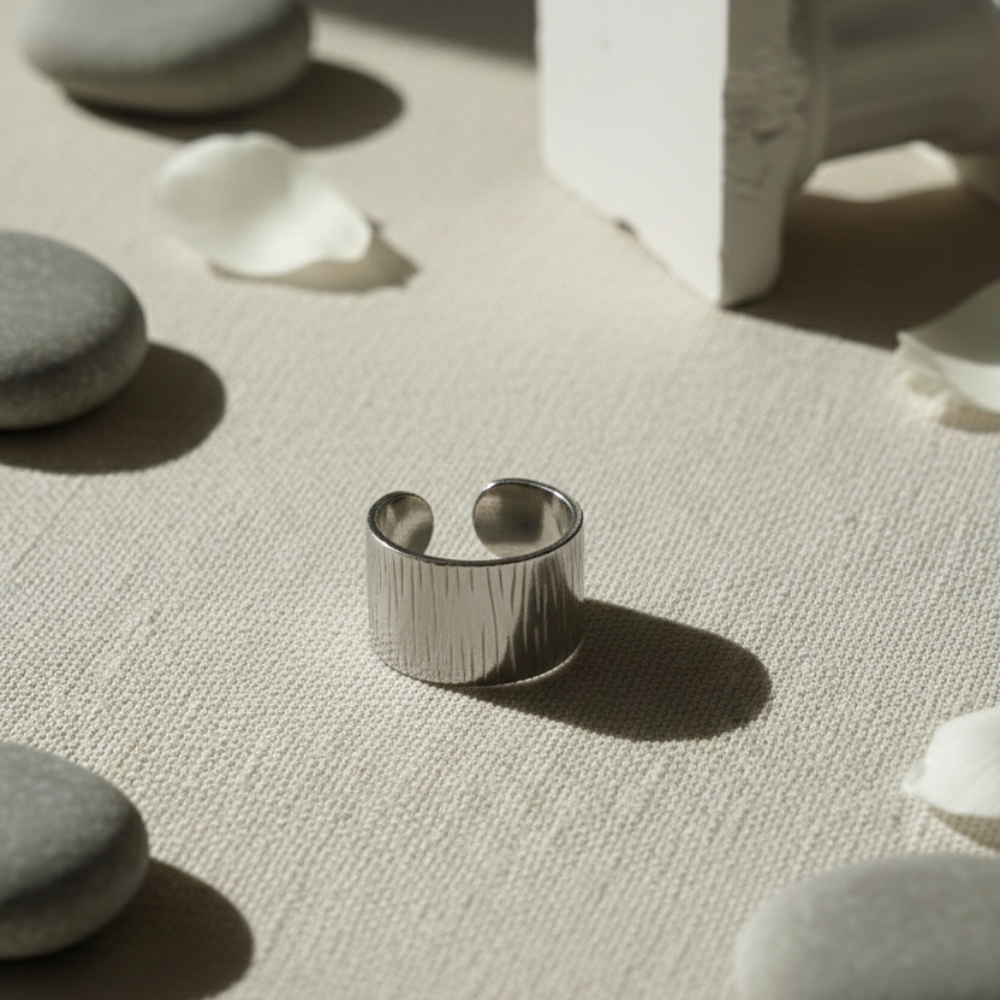 Silver ring on a textured surface with stones and a white object in the background