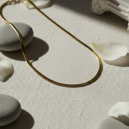 Gold necklace on a textured surface with stones and petals
