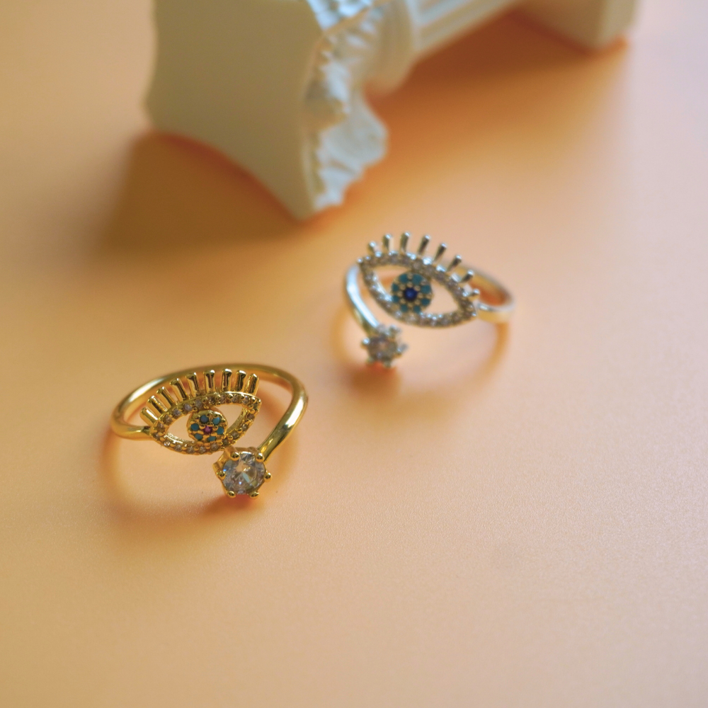 Pair of gold eye-shaped rings on a soft pink background