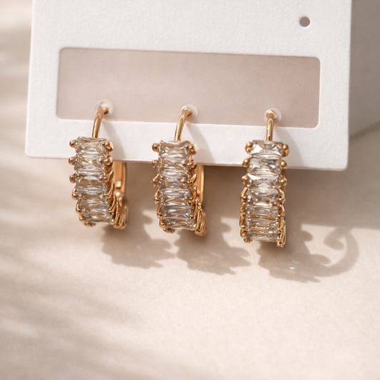 Gold hoop earrings with clear gemstones on a white card against a beige background