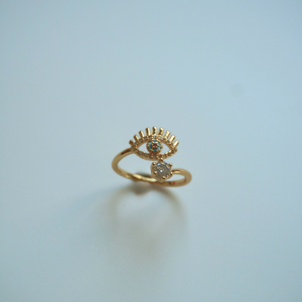 Gold ring with eye design on a light blue background