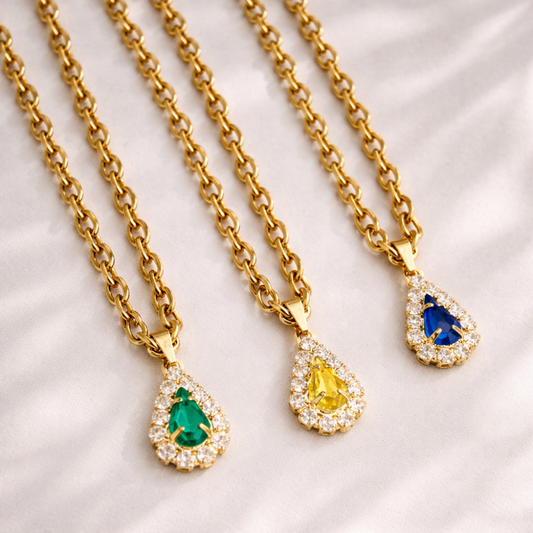 Three gold necklaces with teardrop-shaped gemstones on a white fabric background