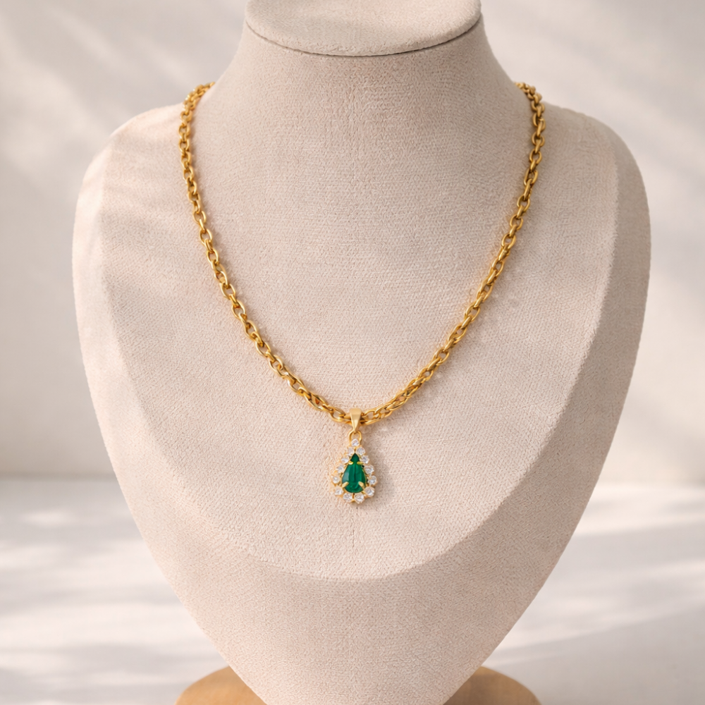 Gold necklace with a green pendant on a mannequin bust against a neutral background