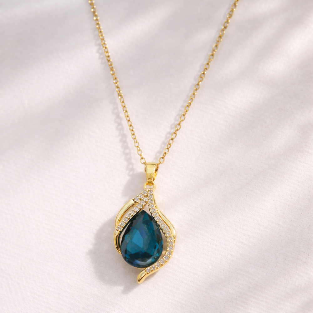 Gold necklace with a blue teardrop pendant on a white background