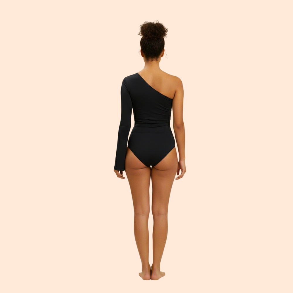 Person wearing a black one-shoulder bodysuit on a beige background