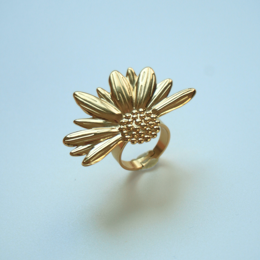 Gold sunflower-shaped ring on a light blue background