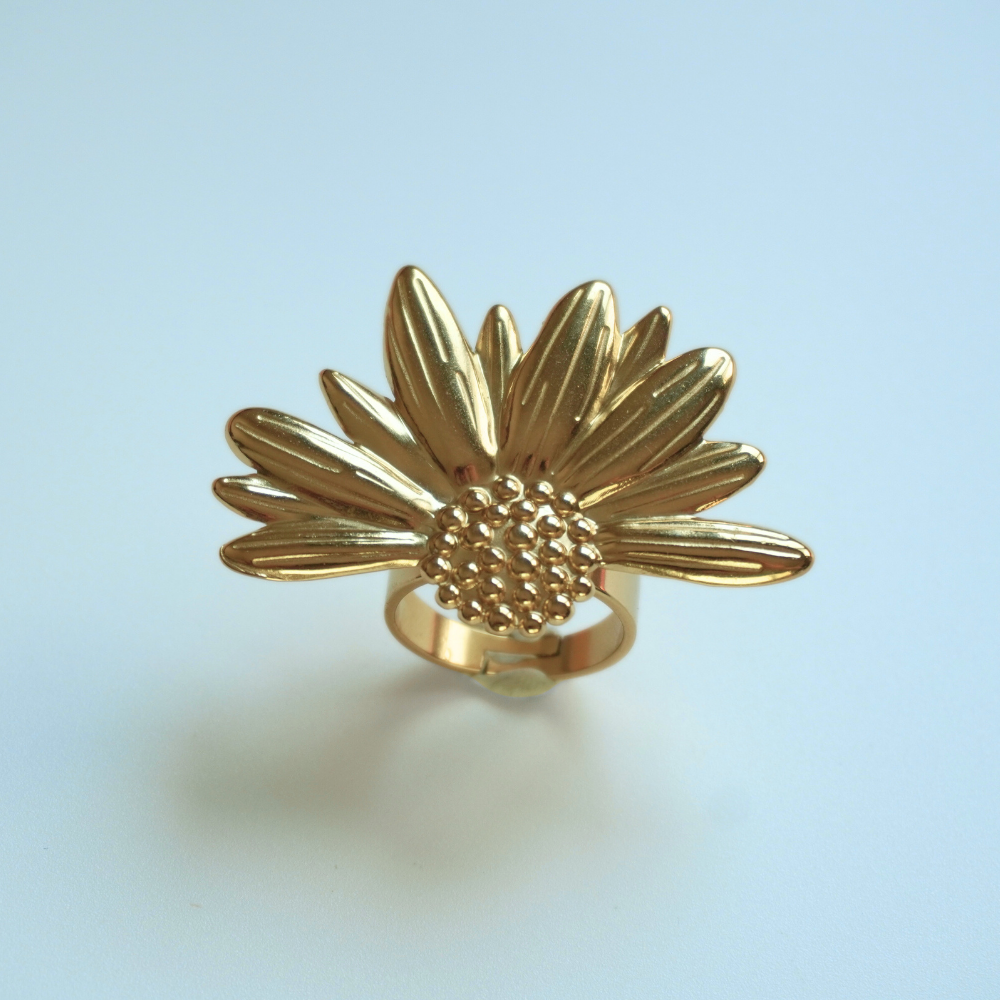 Gold sunflower-shaped ring on a light blue background