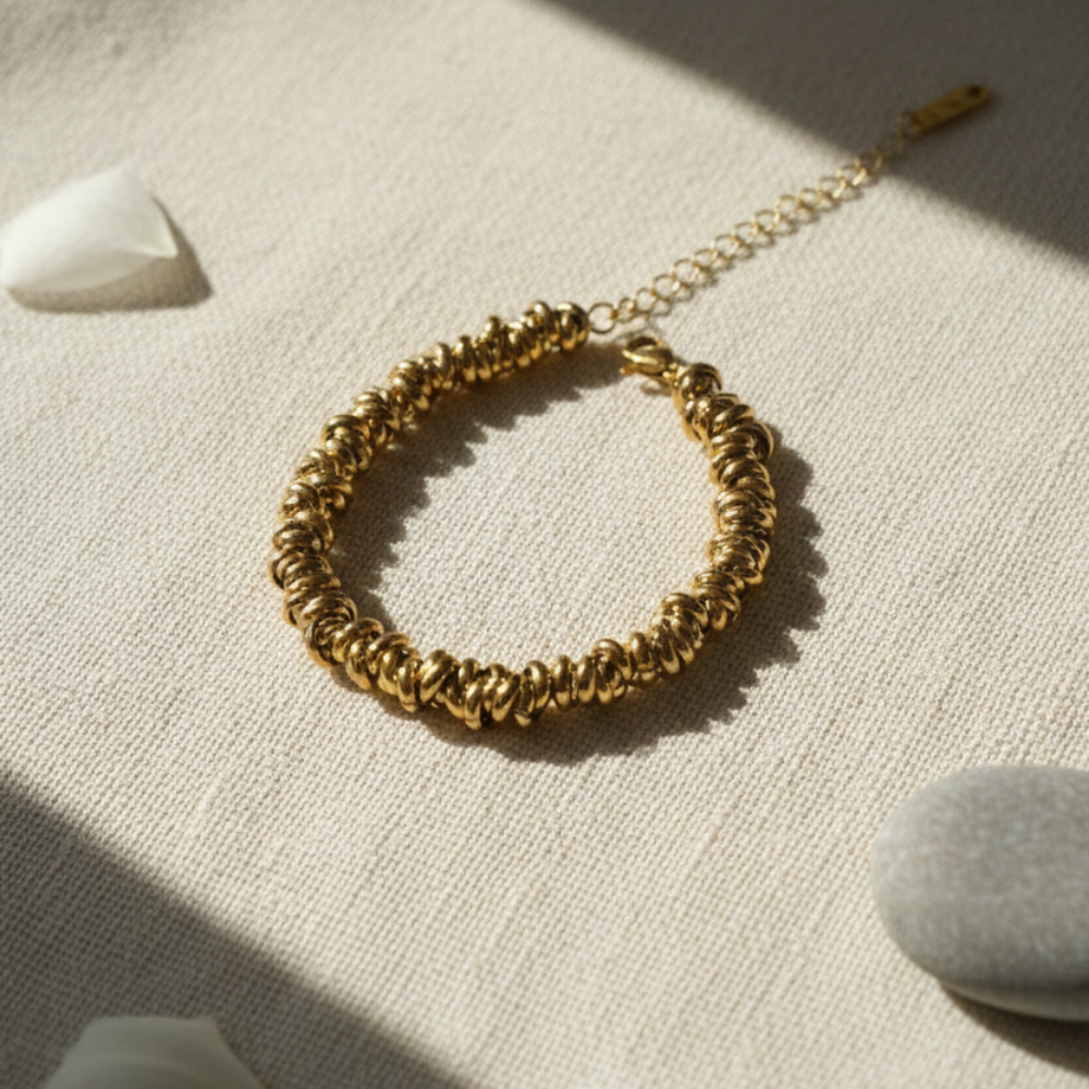 Gold bracelet on a textured beige surface with soft shadows