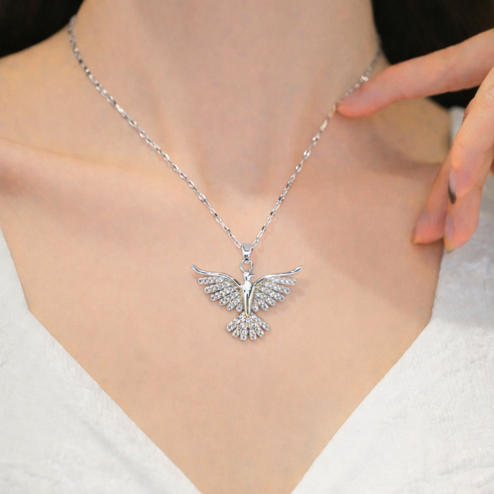 Silver bird pendant necklace on a person wearing a white top.