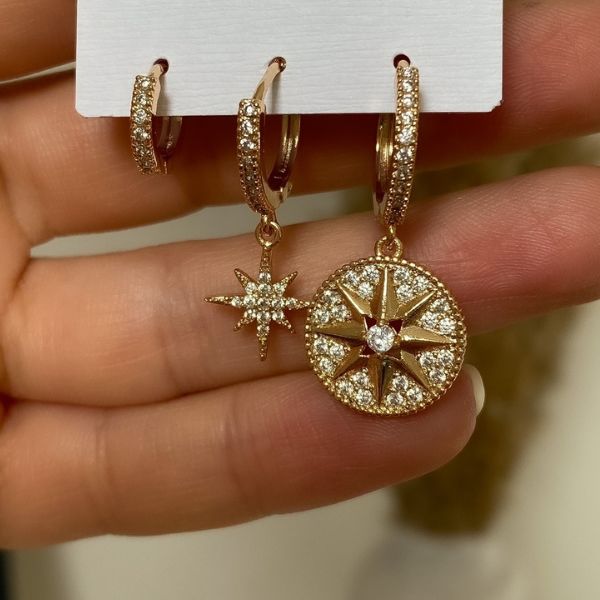 A set of three gold-colored earrings with rhinestone embellishments, displayed on a mannequin hand. The earrings have a star and geometric pattern design.