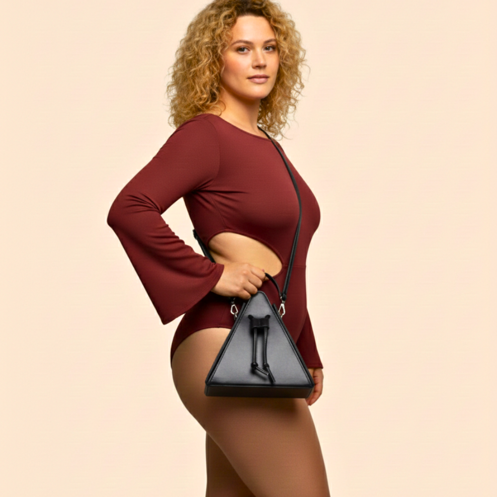 Woman wearing a burgundy outfit holding a black handbag against a beige background