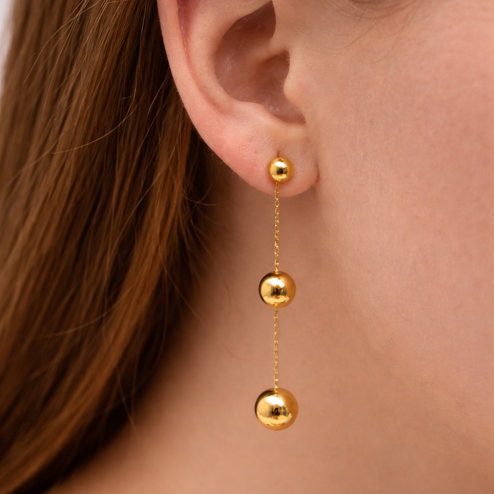 Gold earrings with three spherical beads hanging from an ear.