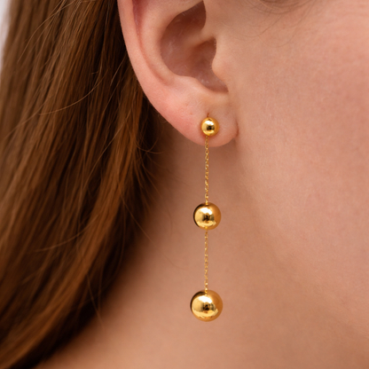 Gold earrings with three spherical beads hanging from an ear.