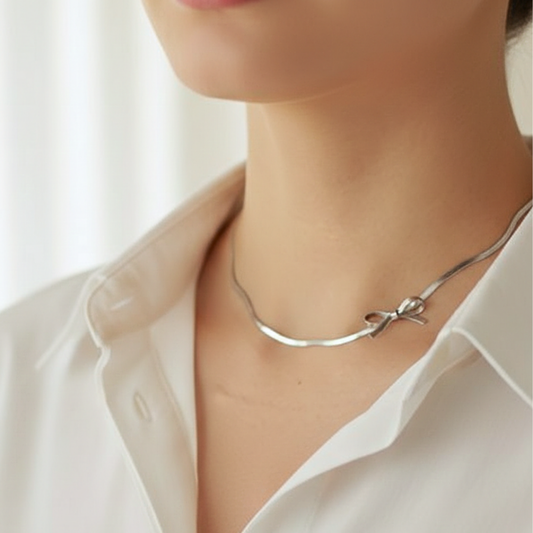Silver necklace with a bow detail worn by a person in a white shirt.