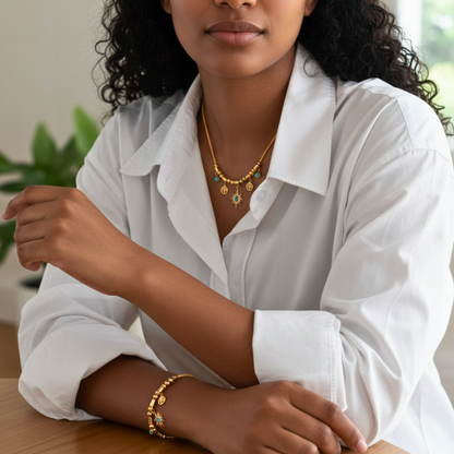 Woman wearing gold jewelry including a necklace and bracelet, sitting indoors.