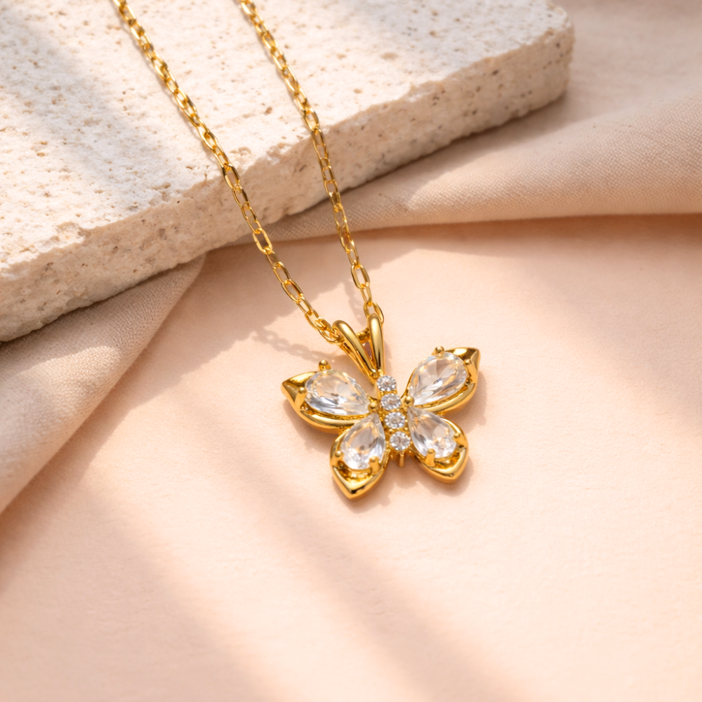 Gold butterfly necklace with clear gemstones on a beige fabric background