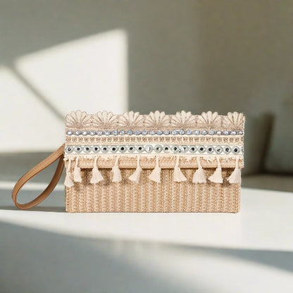 A beige straw square clutch with white lace trim and tassel detailing, displayed against a shadowed background.
