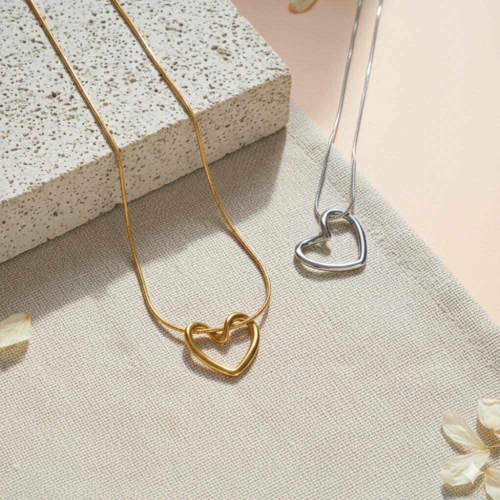 Gold and silver heart-shaped necklaces on a textured surface with flowers.