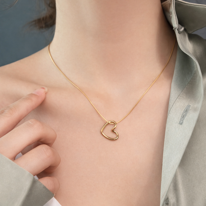 Gold heart-shaped necklace on a person wearing a light gray shirt.