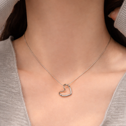 Silver heart-shaped necklace on a person wearing a gray sweater.