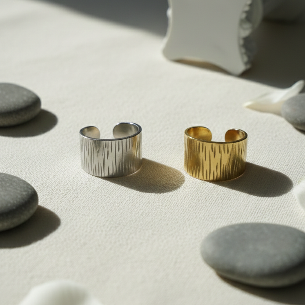 Gold and silver rings on a textured surface with stones and a white object in the background