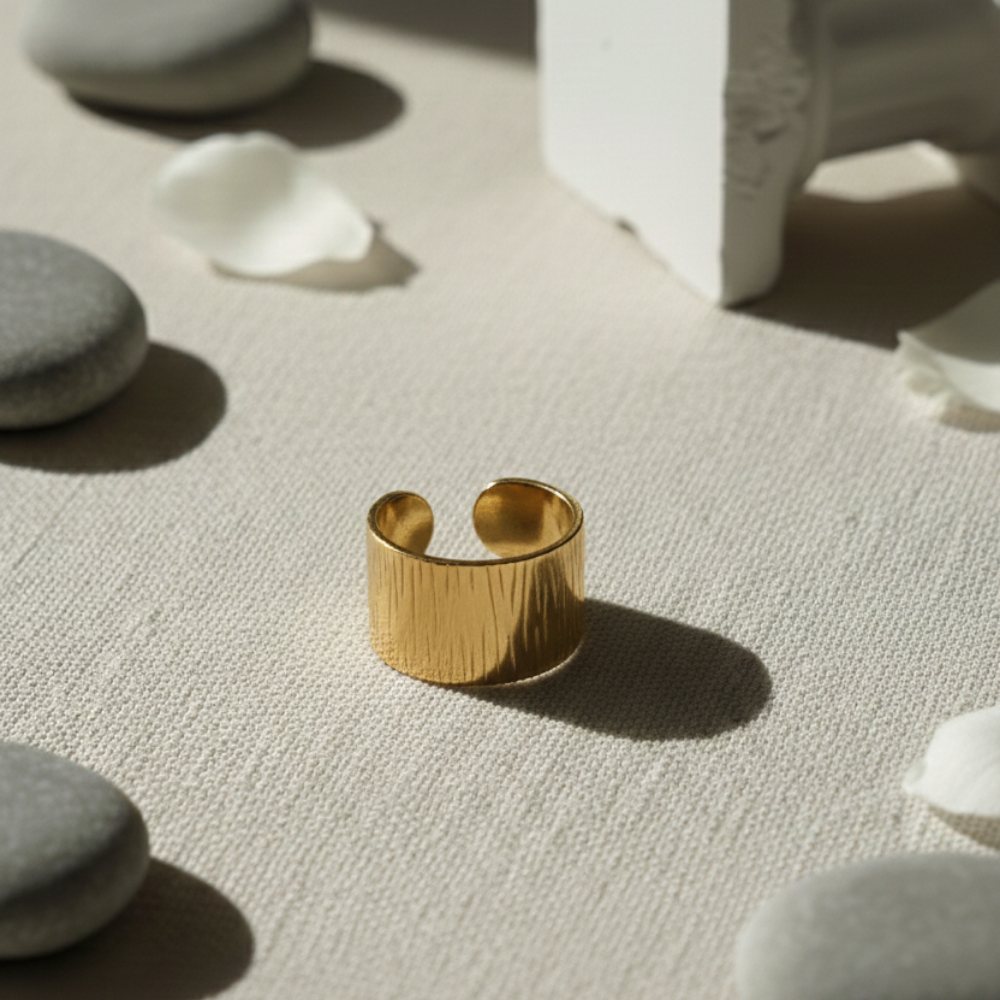Gold ring on a textured surface with stones and a white object in the background