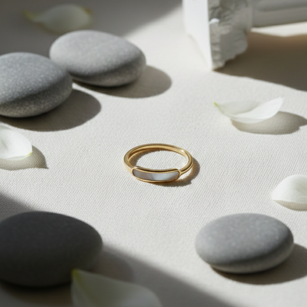 Gold ring on a white surface with gray stones and white petals