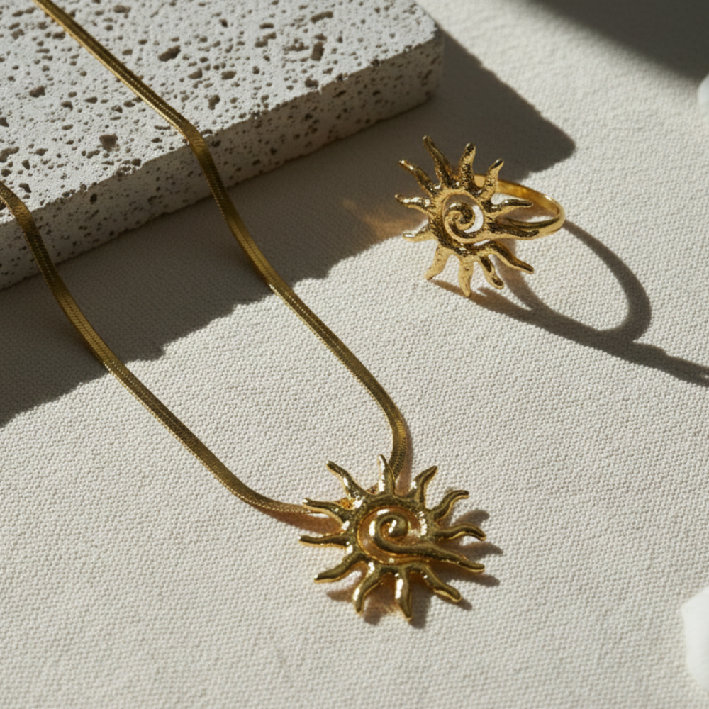 Gold sun-shaped necklace and ring on a textured surface