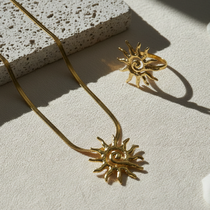 Gold sun-shaped necklace and ring on a textured surface