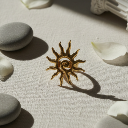 Bronze sun-shaped object on a textured surface with stones and petals