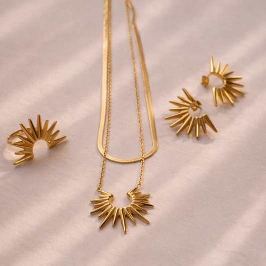 Gold necklace and earrings set on a soft pink background