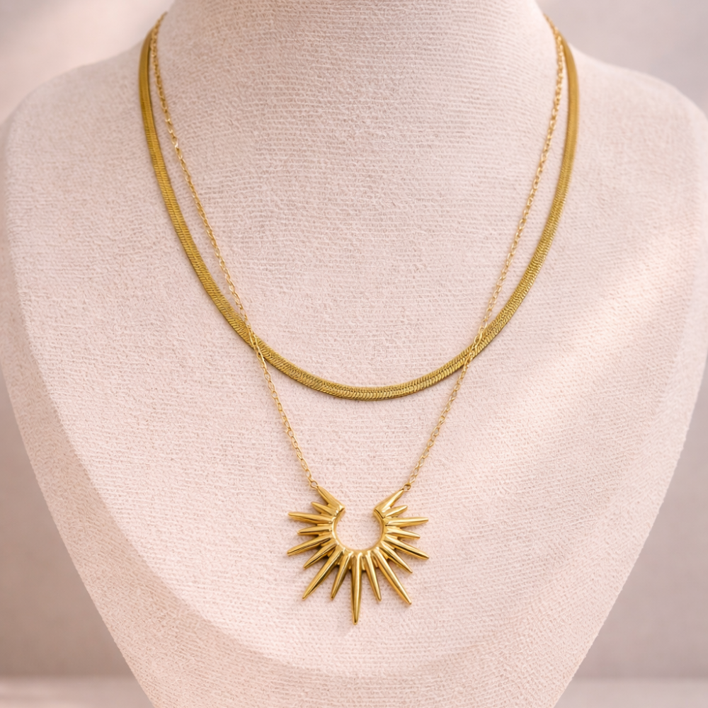Gold necklace with a sunburst pendant on a mannequin bust.