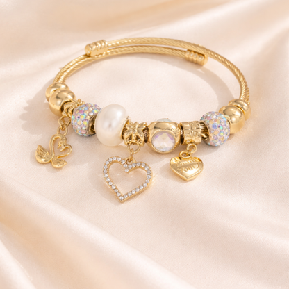 Gold bracelet with heart and butterfly charms on a soft pink background