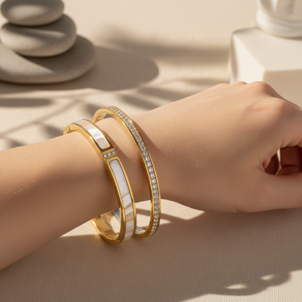 Hand wearing two gold bracelets on a neutral background