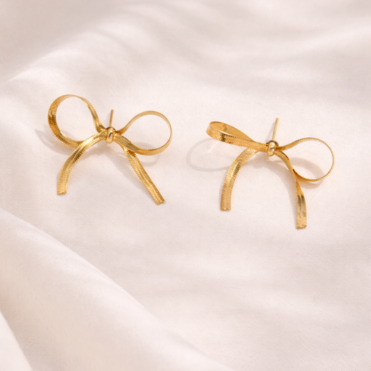 Gold bow-shaped earrings on a soft white background