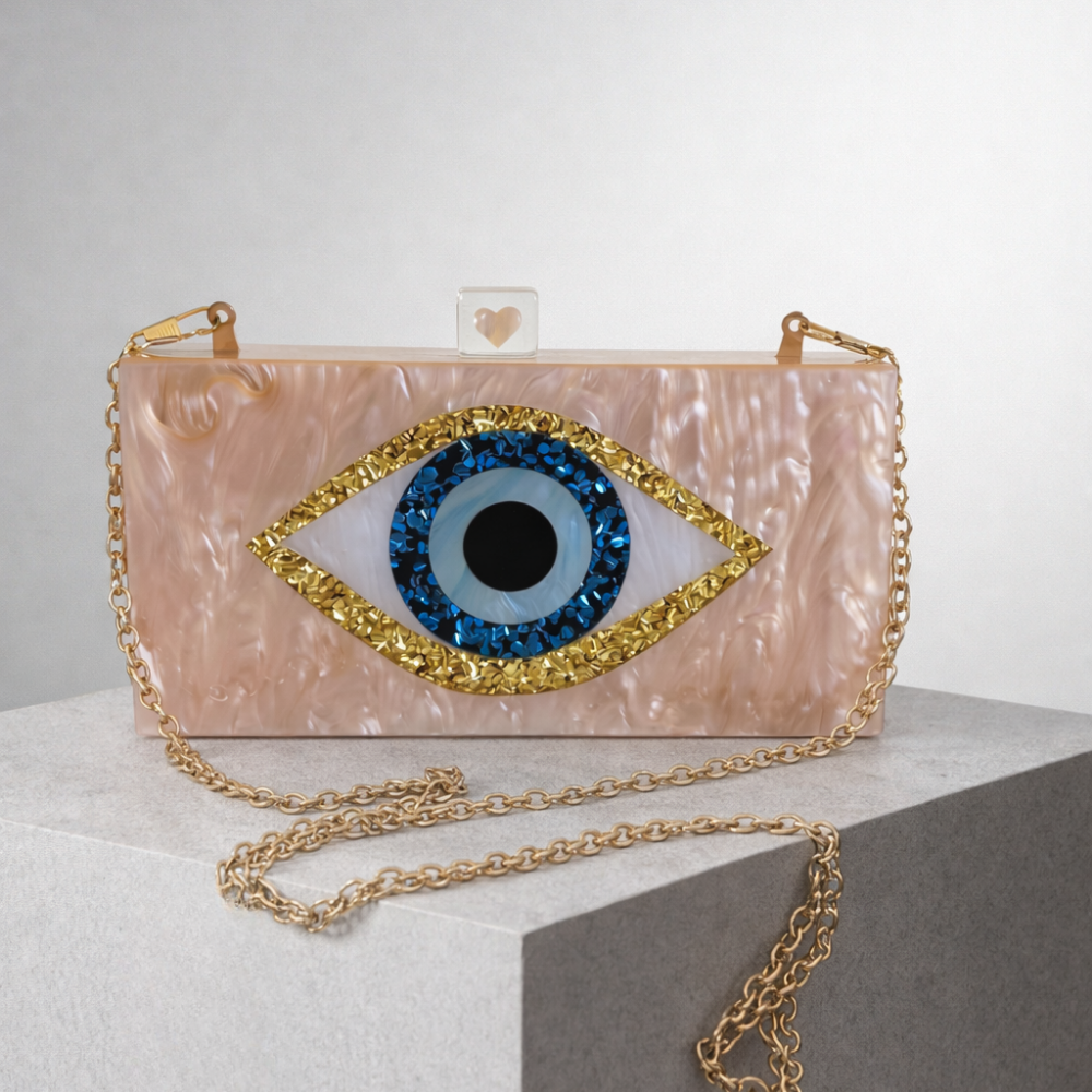 Pink clutch with eye design and gold chain on a white surface