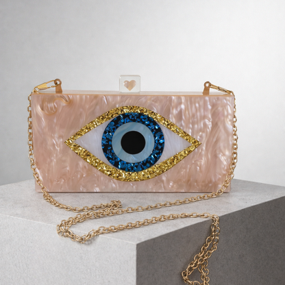 Pink clutch with eye design and gold chain on a white surface