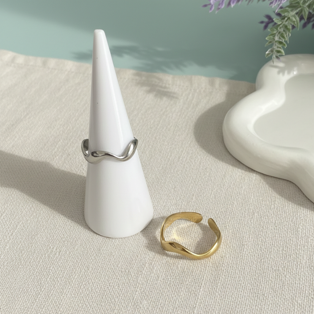 Two rings, one silver and one gold, on a white cone-shaped stand with a light background.