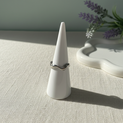 Silver ring on a white cone-shaped stand with a light background
