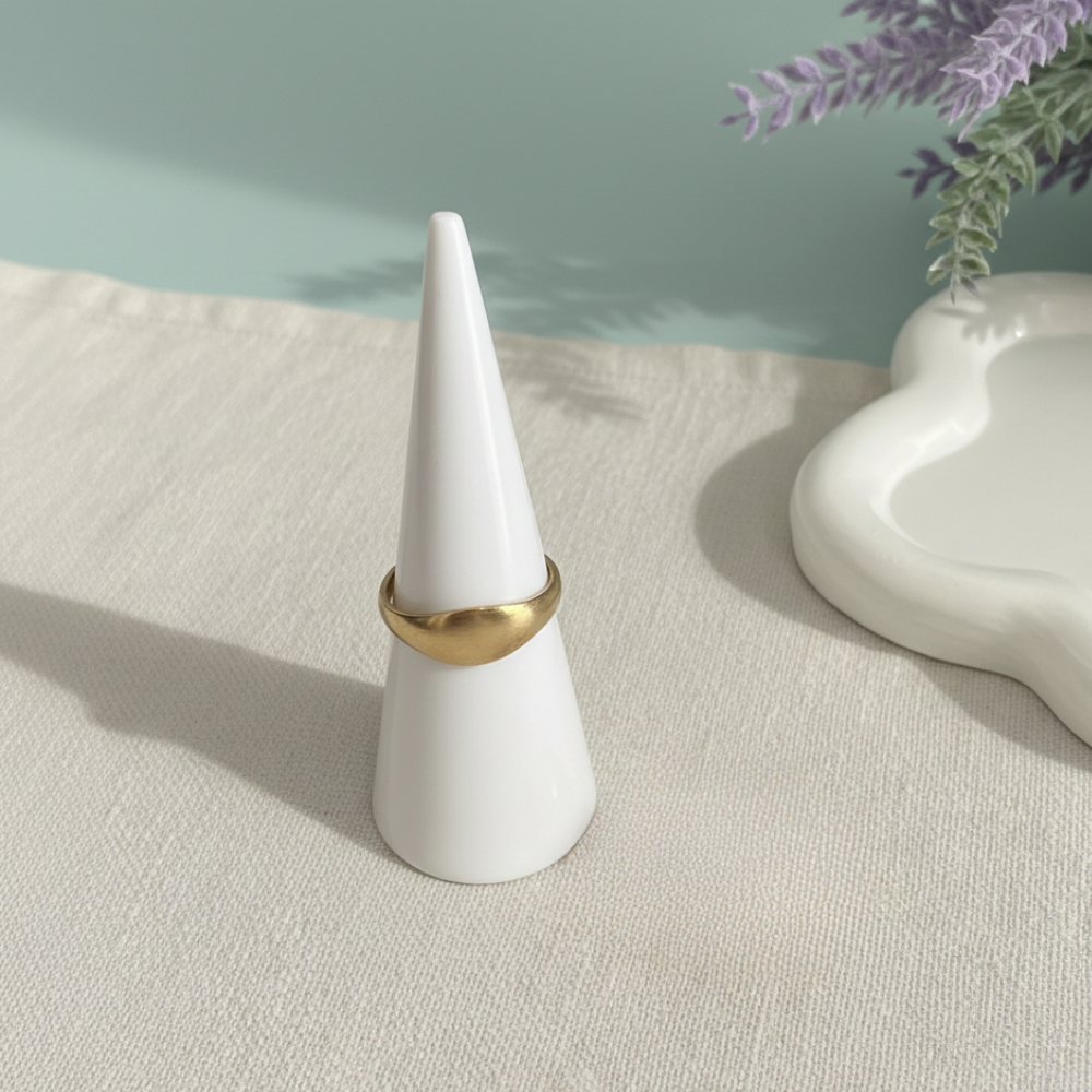 Gold ring on a white cone-shaped stand with a light background