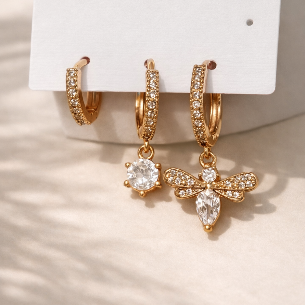 Gold hoop earrings with diamond-like stones on a white card against a beige background