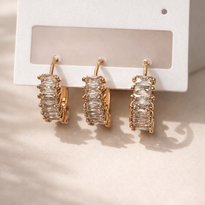 Gold hoop earrings with clear gemstones on a white card against a beige background