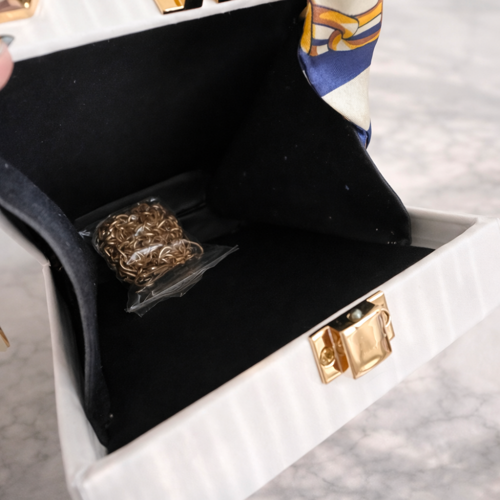White jewelry box with gold clasp and black interior, containing a gold chain.