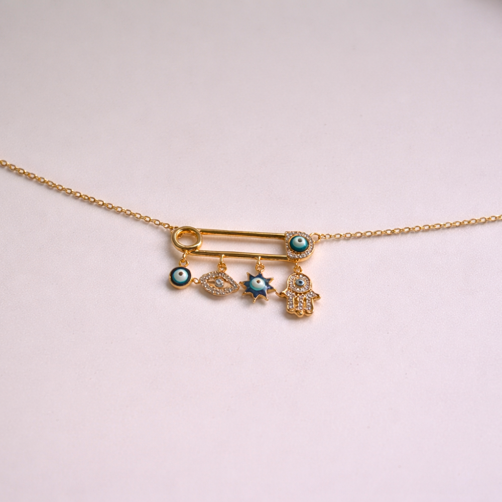 Gold necklace with safety pin charms on a light pink background