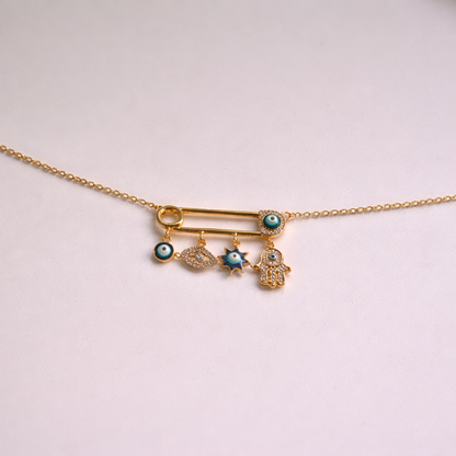 Gold necklace with safety pin charms on a light pink background