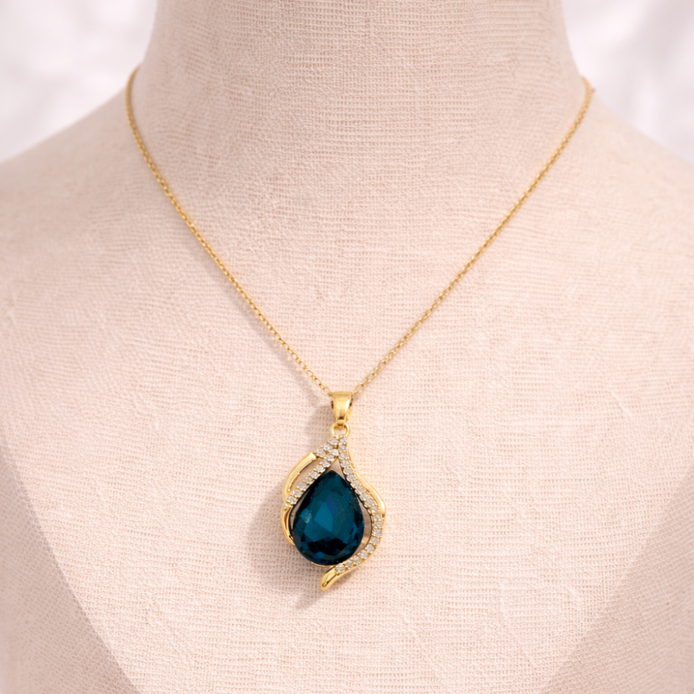 Gold necklace with a blue teardrop pendant on a mannequin.