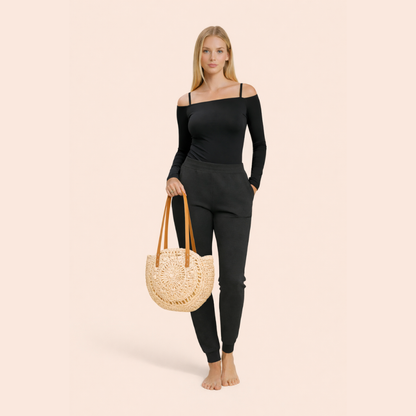Woman in black outfit holding a straw bag on a beige background