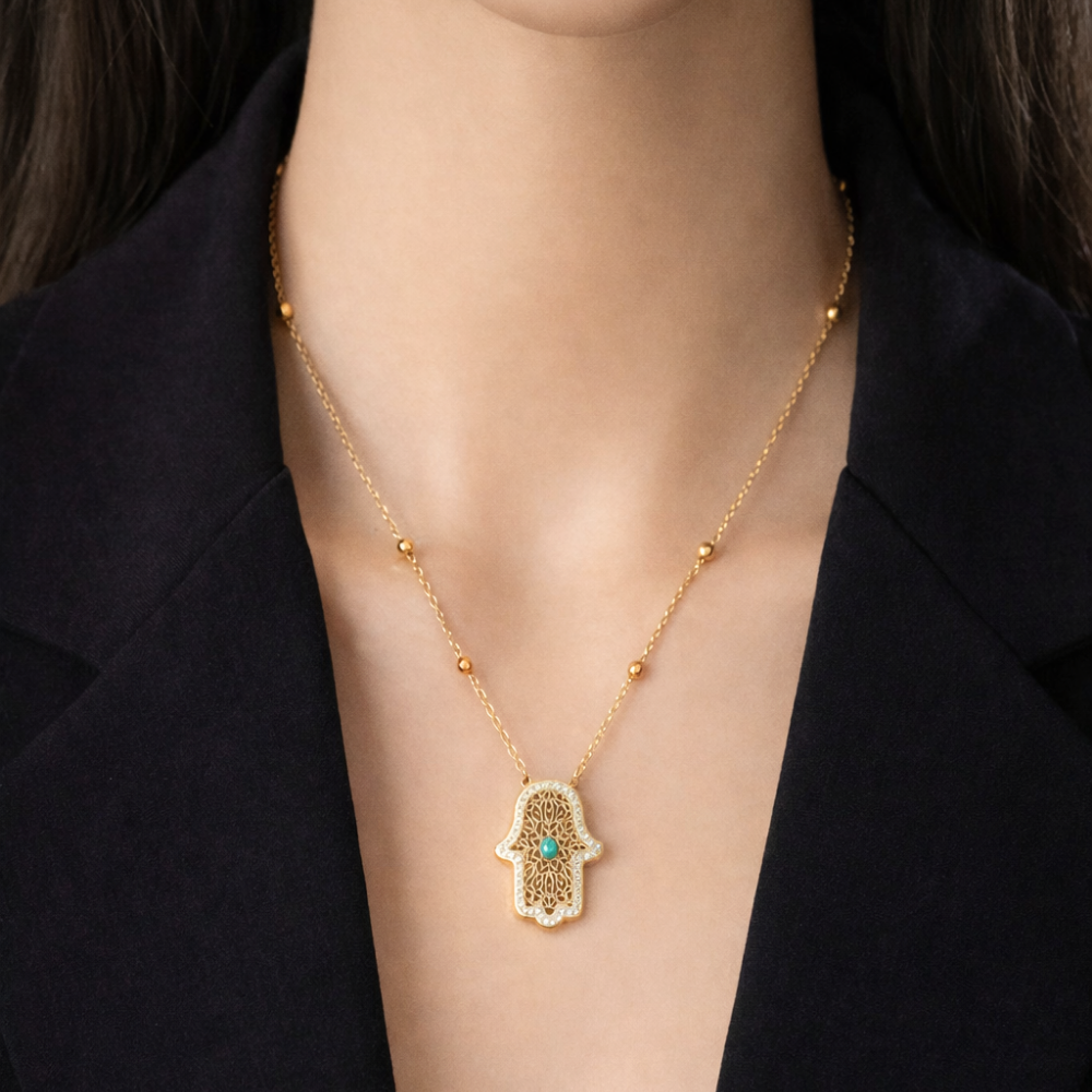 Gold necklace with a Hamsa hand pendant on a person wearing a black blazer.