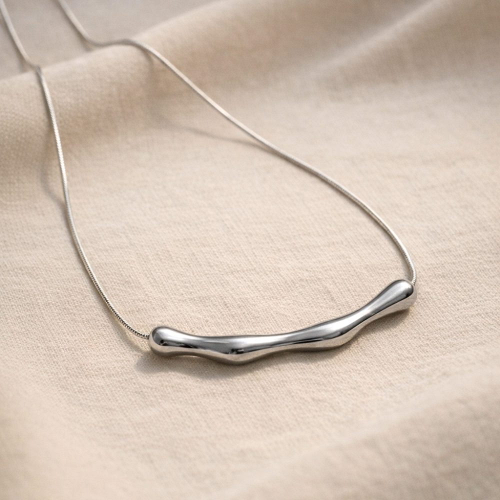 Silver necklace with a wavy design on a beige fabric background