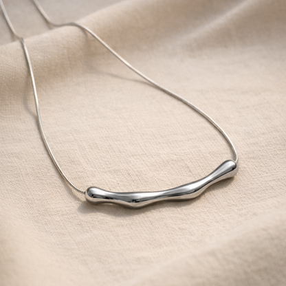 Silver necklace with a wavy design on a beige fabric background
